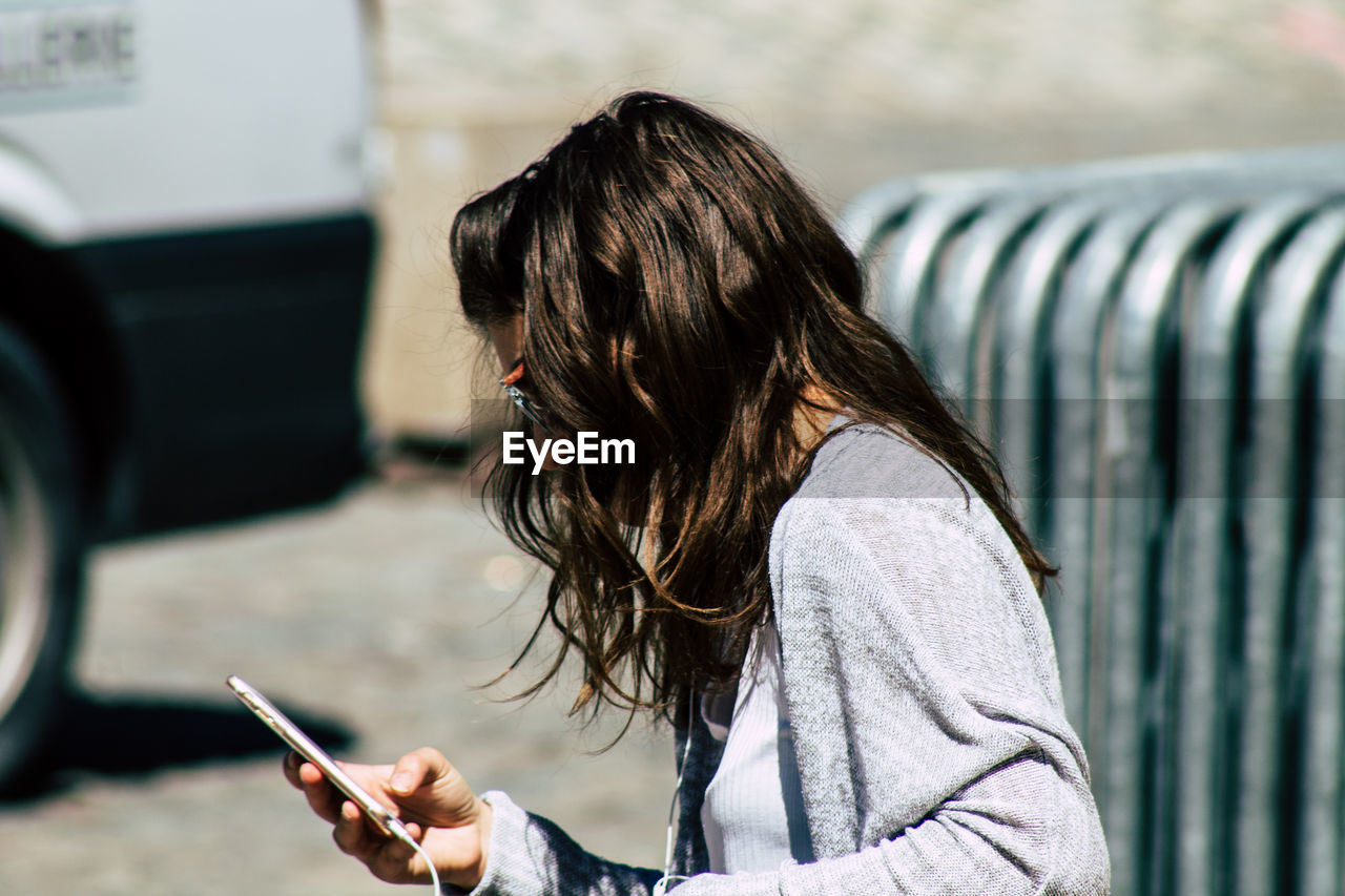 SIDE VIEW OF WOMAN USING SMART PHONE OUTDOORS