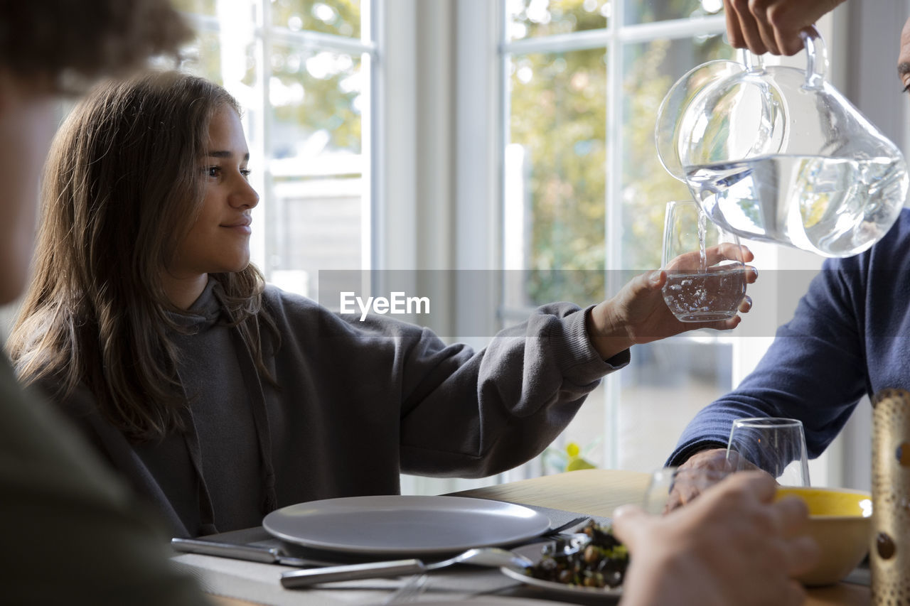 Cropped hand of boy pouring water for sister in glass during dinner