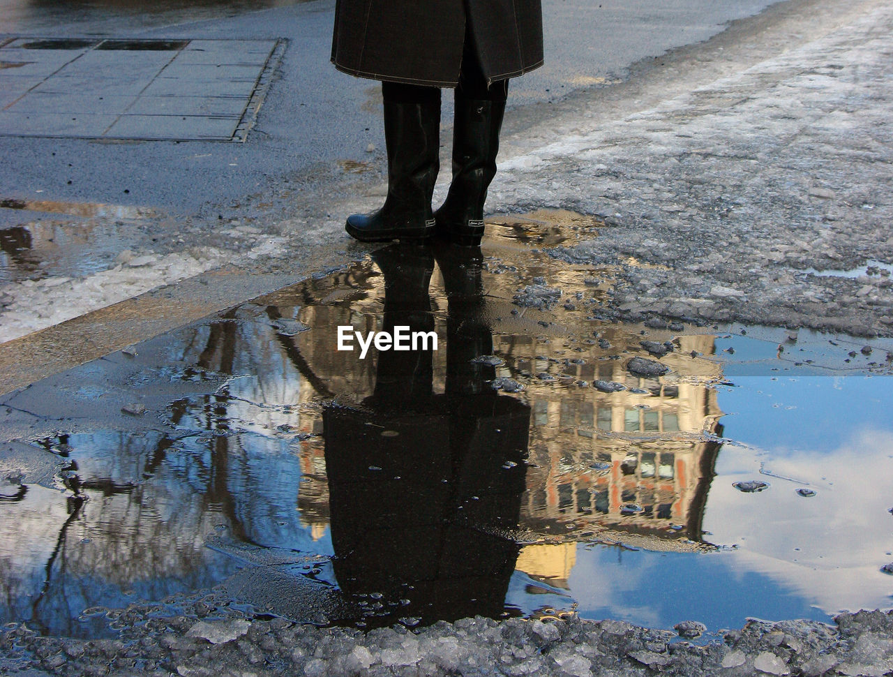 Low section of person reflecting in puddle on street