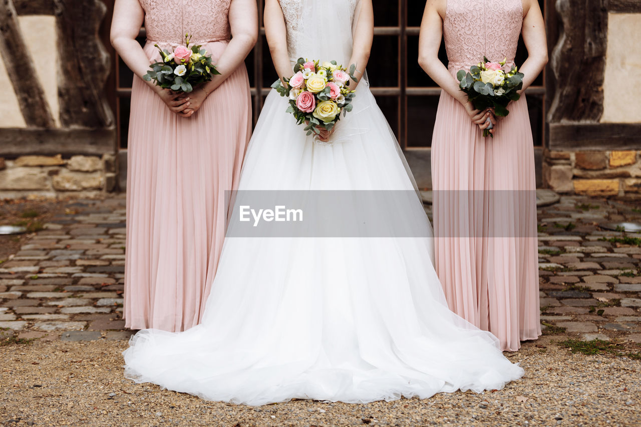 The bride and bridesmaids in an elegant dress is standing and holding hand bouquets of pastel pink 