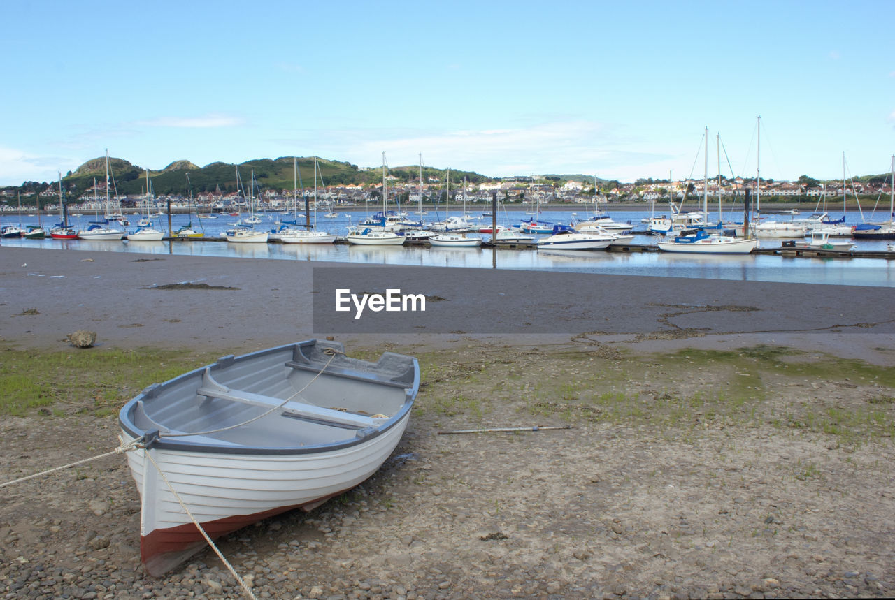 Sailboats moored on shore against blue sky