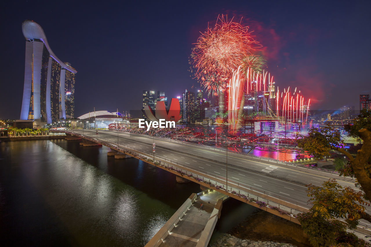 Firework display over river and illuminated buildings in city at night