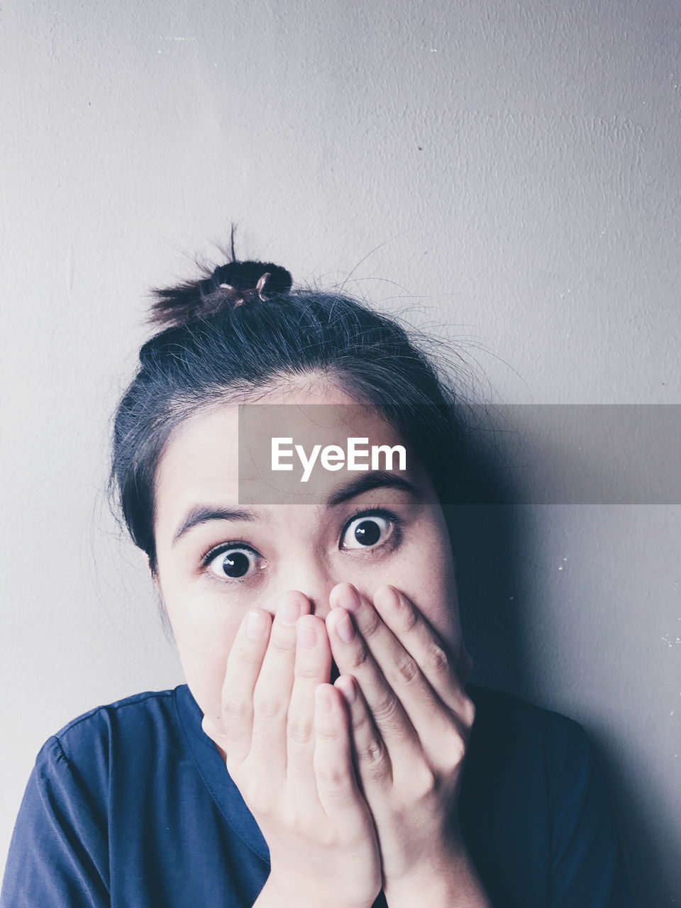 Portrait of surprised young woman hands covering mouth against wall