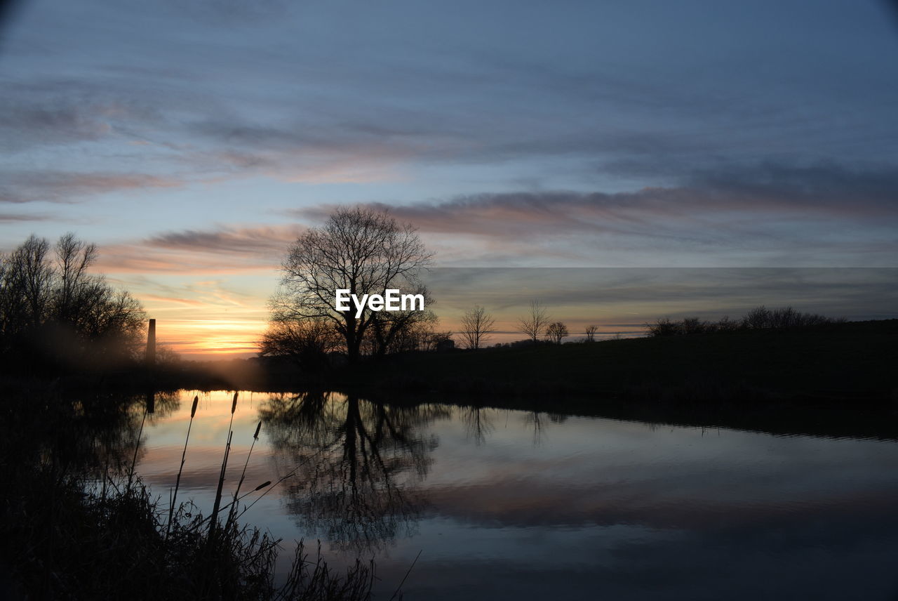 REFLECTION OF SILHOUETTE TREES IN LAKE AGAINST SKY DURING SUNSET