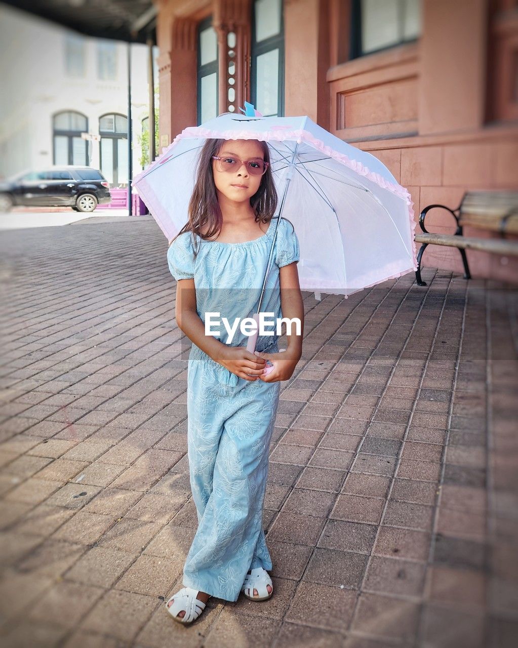 portrait of young woman with umbrella standing on footpath in city