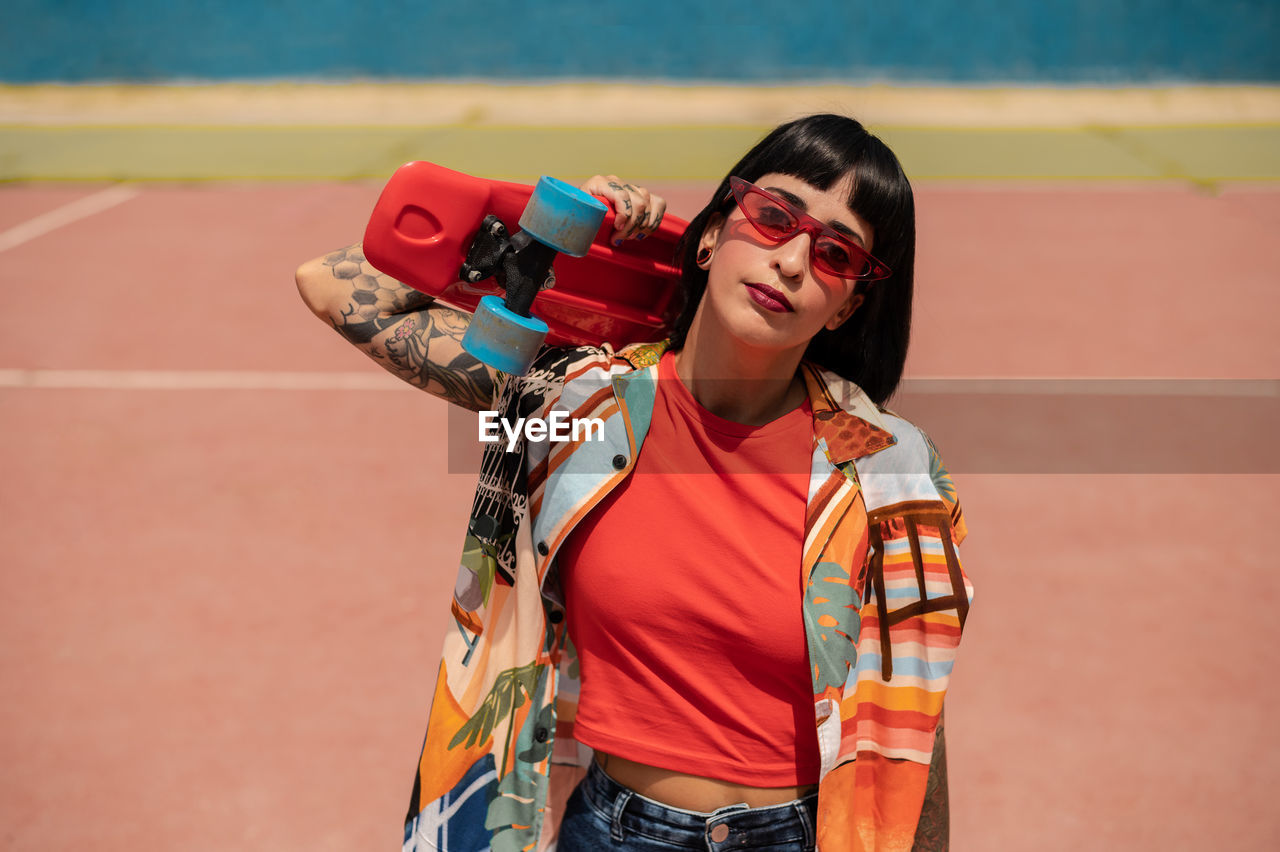 Caucasian girl with tattoos and short black hair on a sports ground with a skateboard in her hands