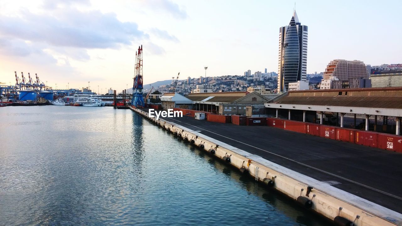 High angle view of cranes and buildings at harbor against sky