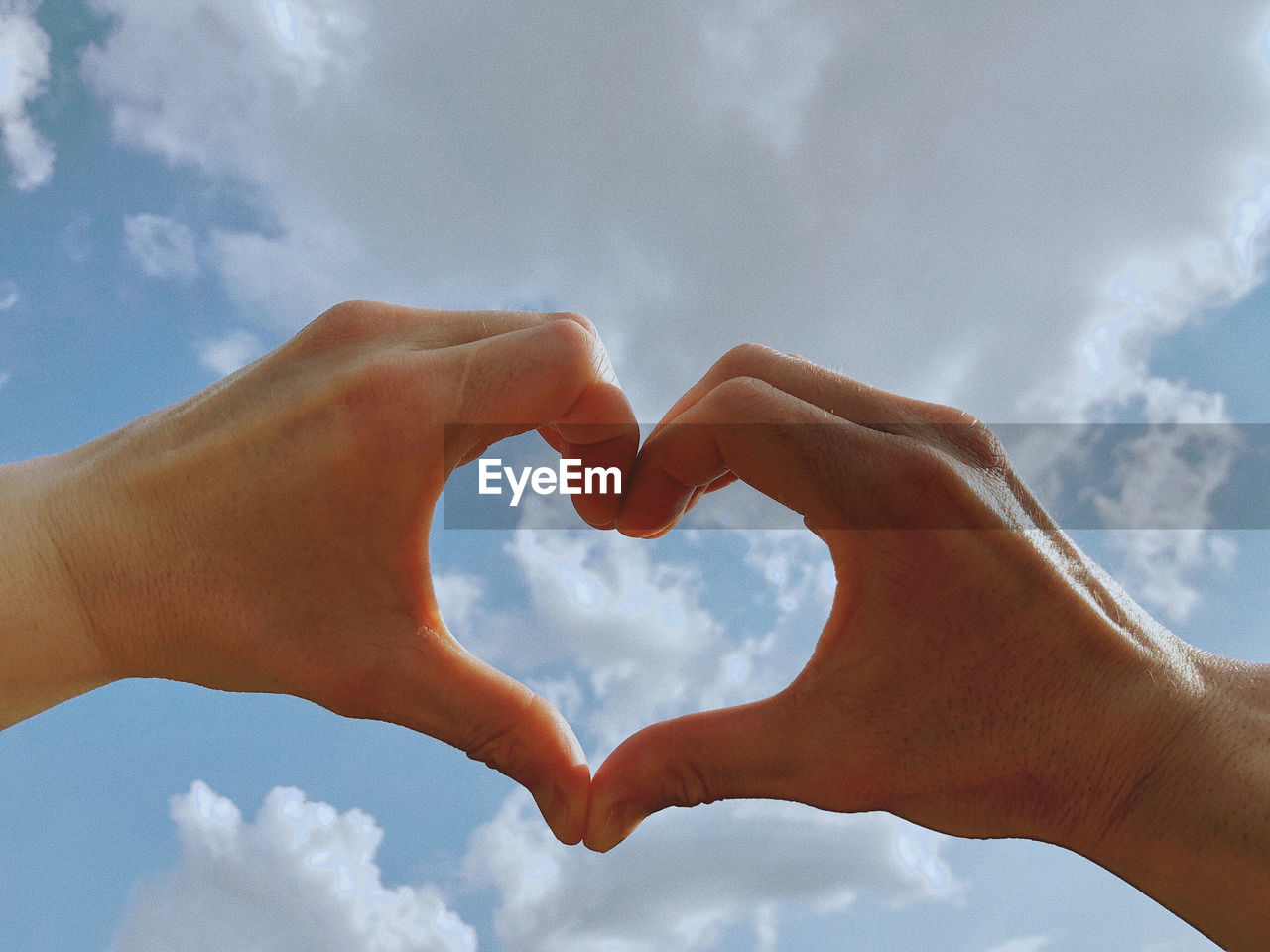 Cropped image of hand holding heart shape against sky