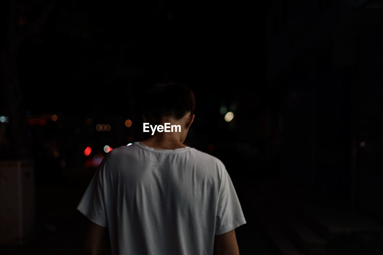 REAR VIEW OF A MAN STANDING IN ILLUMINATED NIGHT