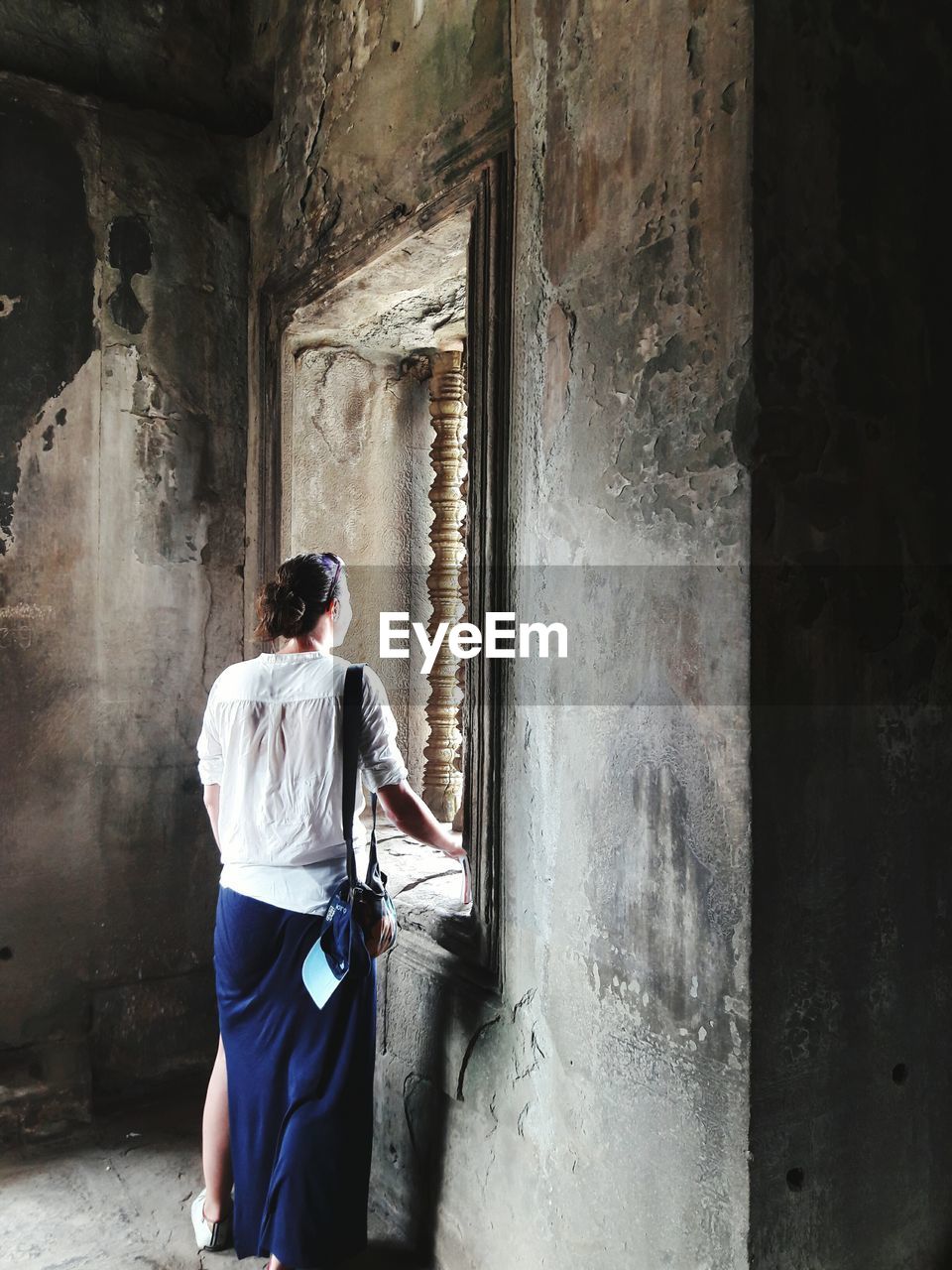 Rear view of woman standing by window in abandoned building