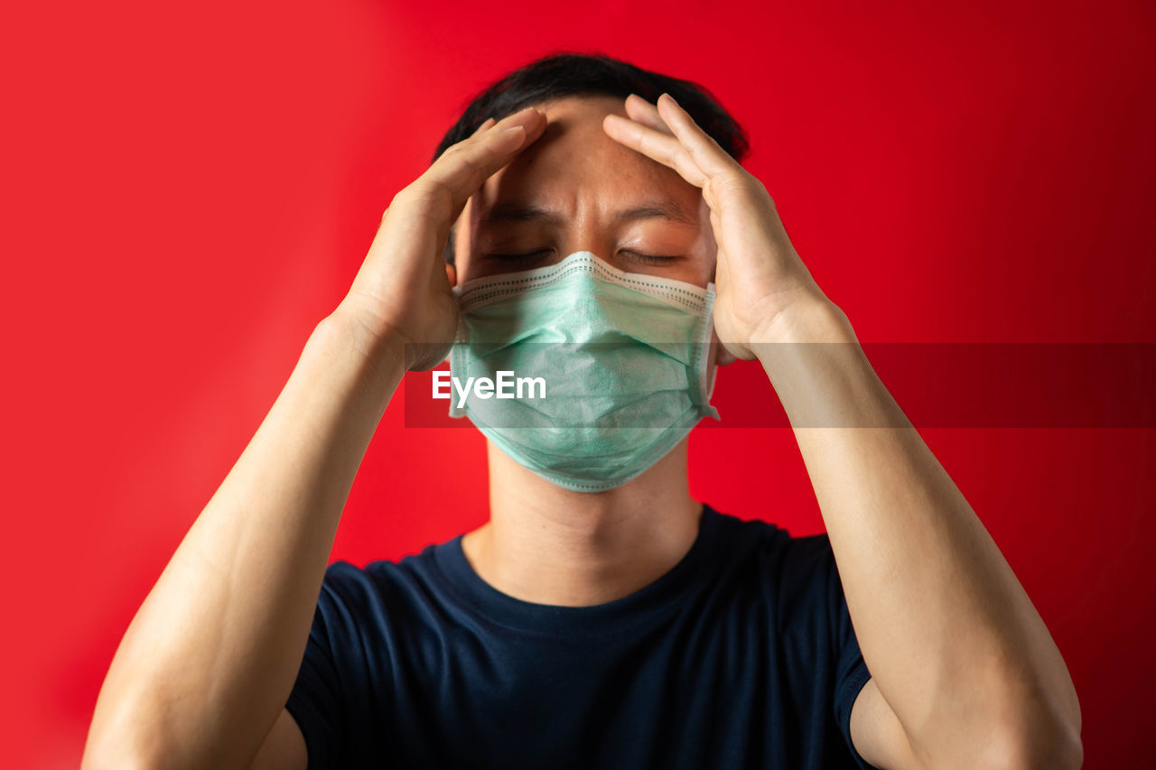 Close-up of man with mask suffering from headache against red background