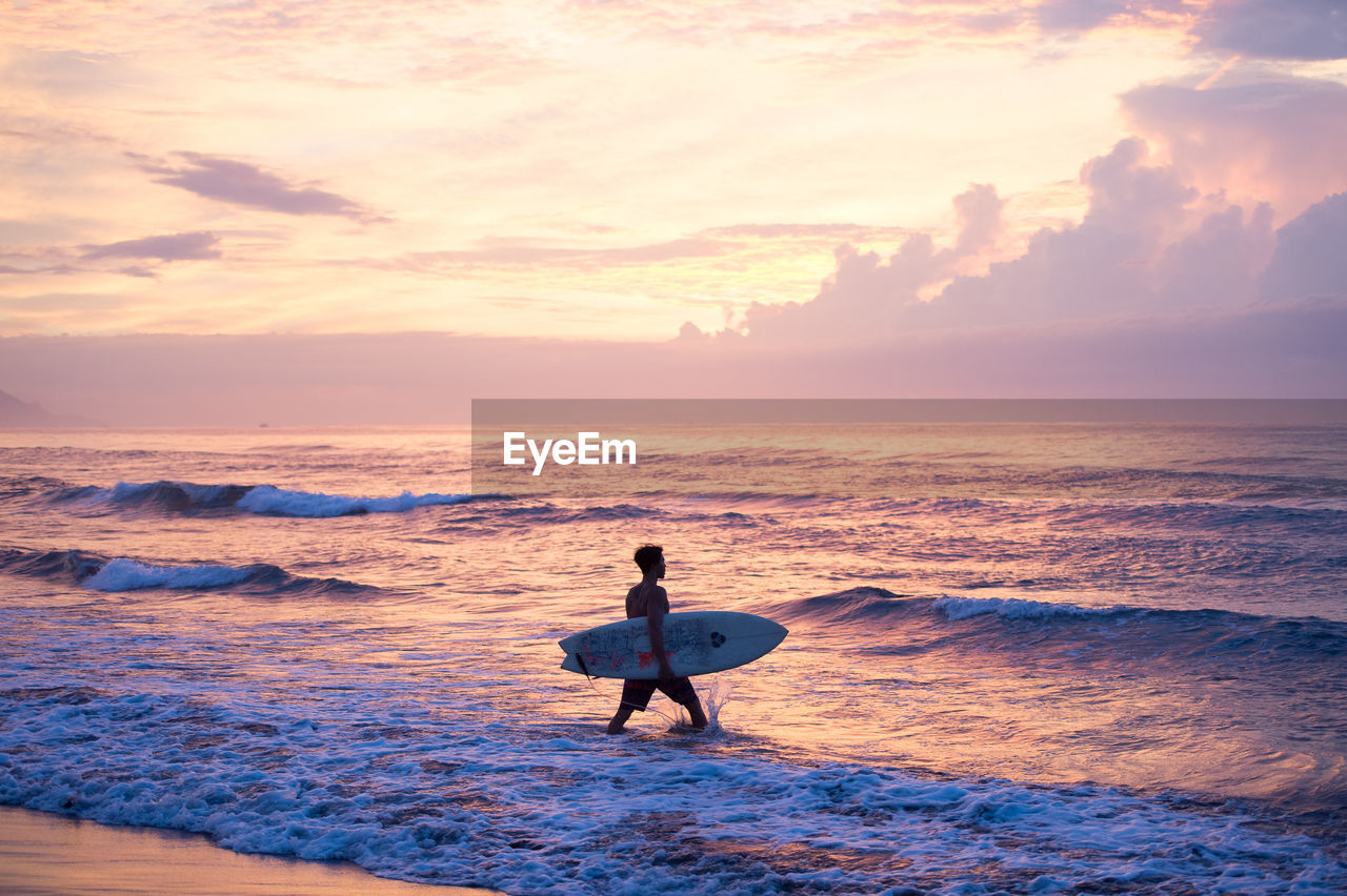 Surfer on beach against sky during sunset