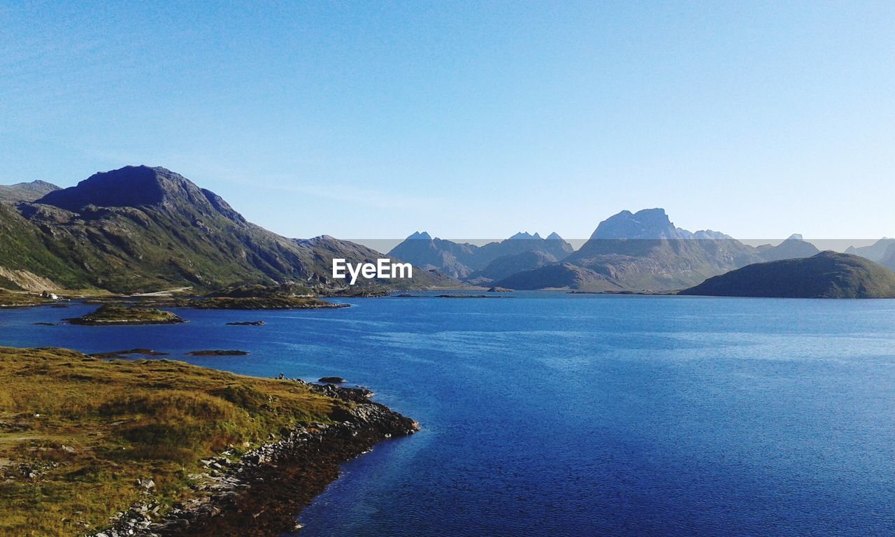 Scenic view of sea and mountains against clear blue sky