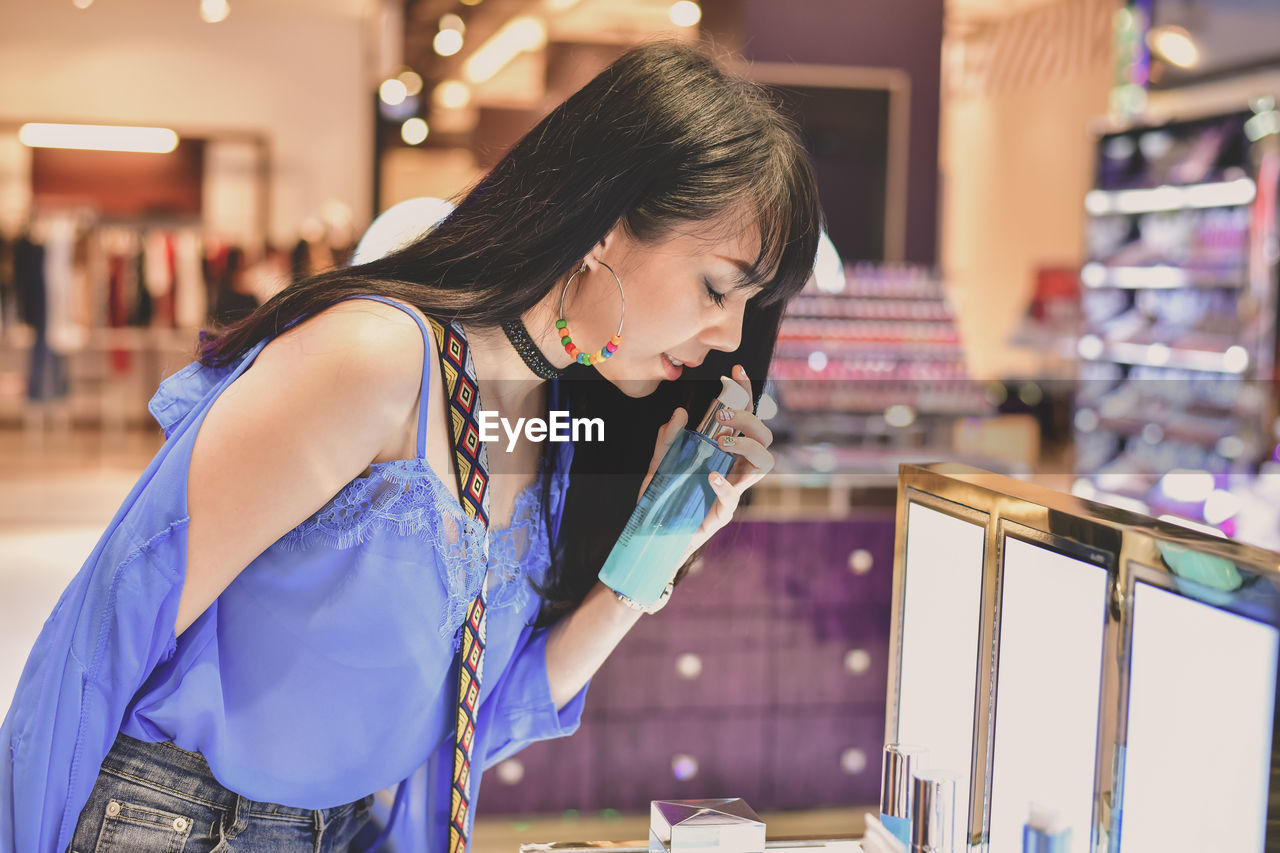 Young woman smelling perfume in store