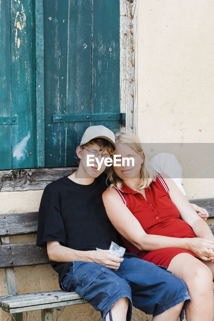 Portrait of mother and son sitting on bench against window