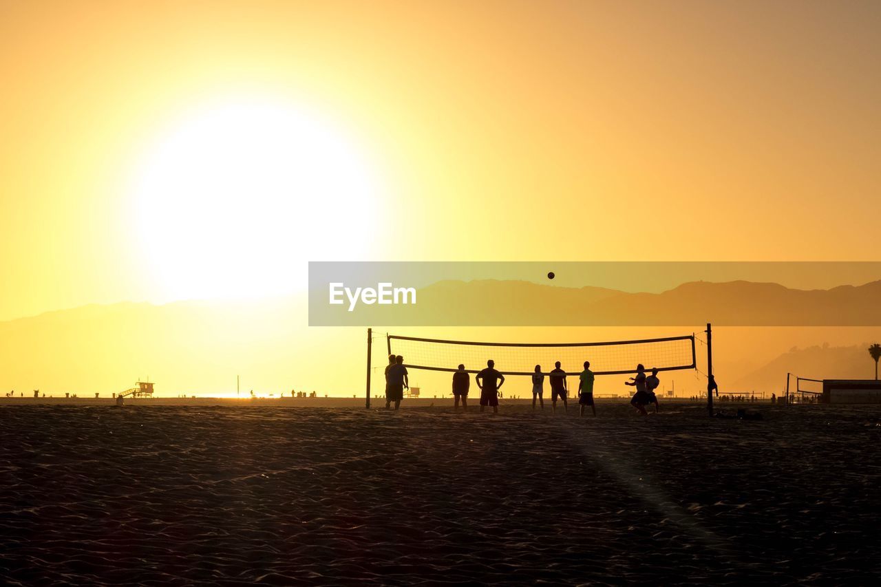 People playing volleyball at beach against sky during sunset