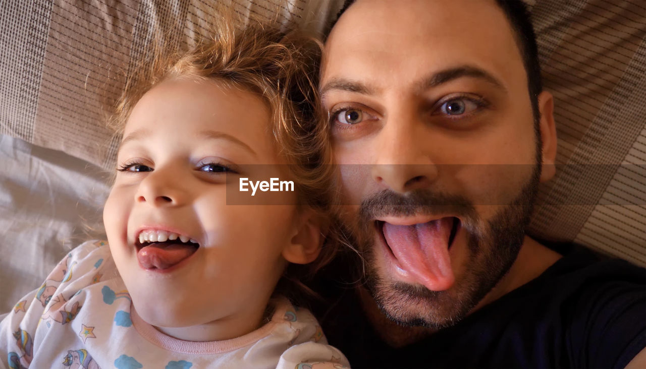 Portrait of father and daughter lying on bed at home