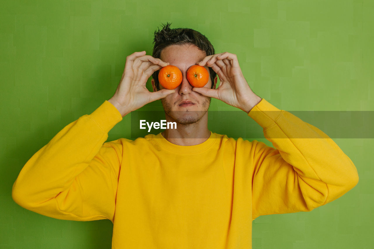 Young boy joking with two oranges in his eyes on a green background