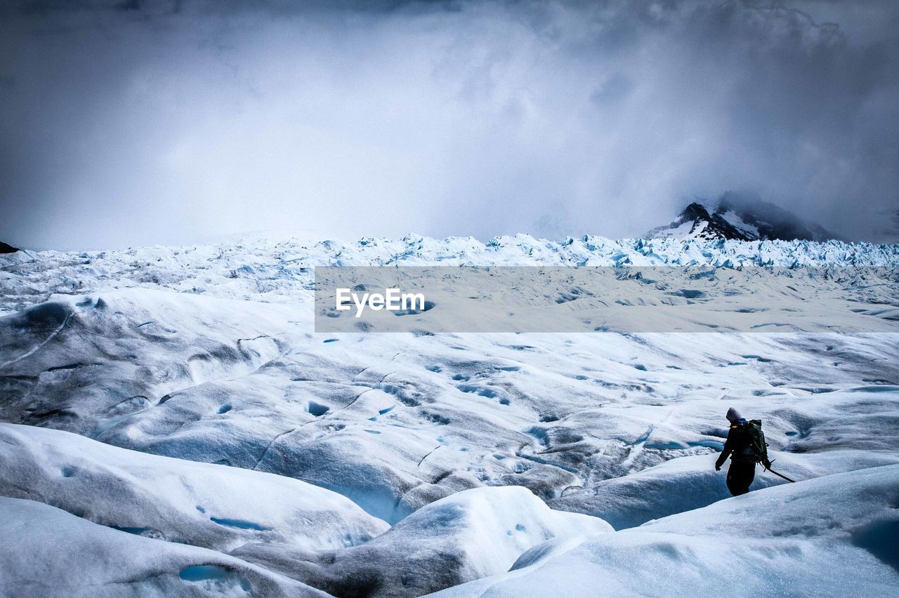 Person walking on glacier landscape against sky
