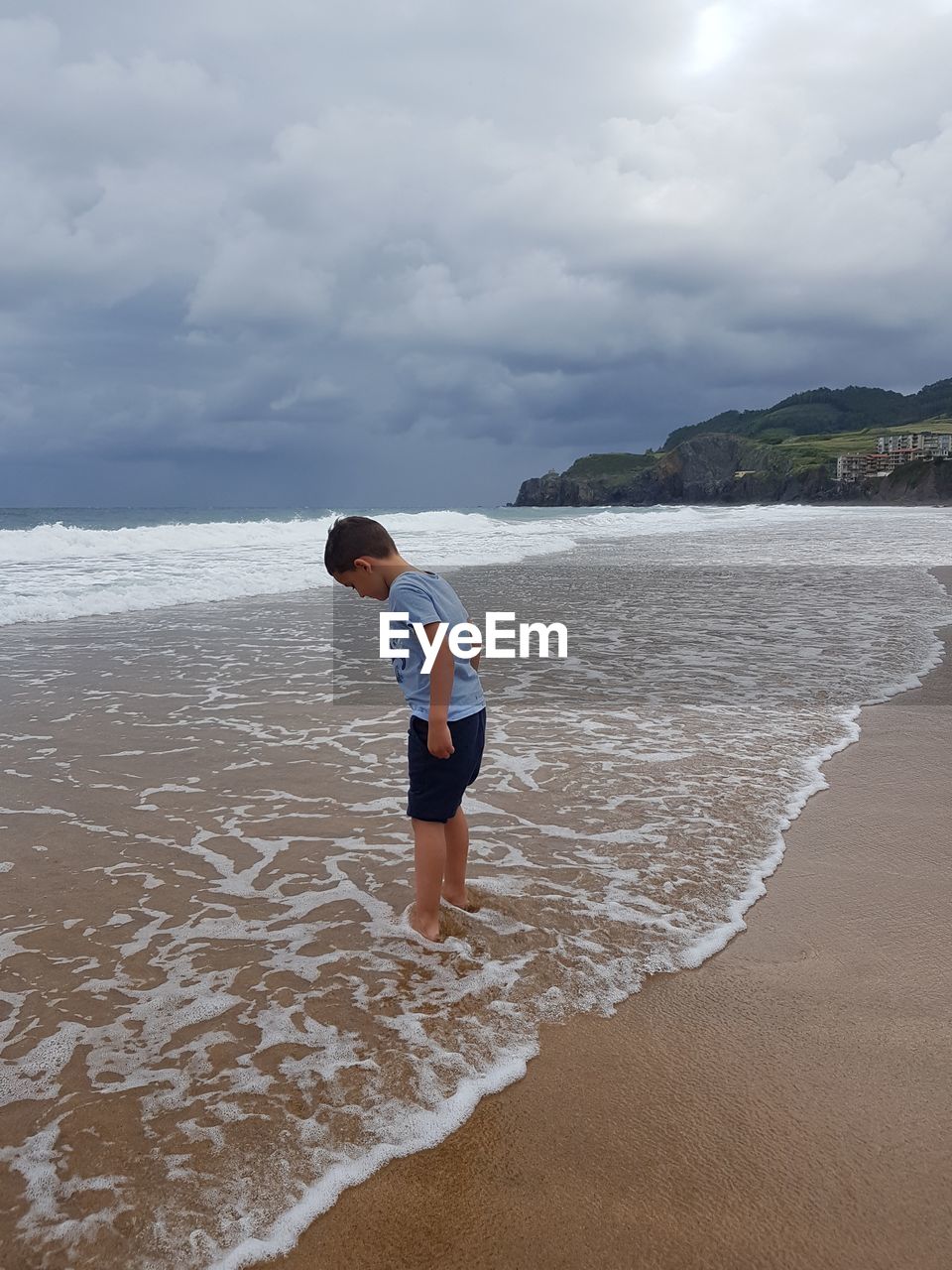 Child standing on beach against sky