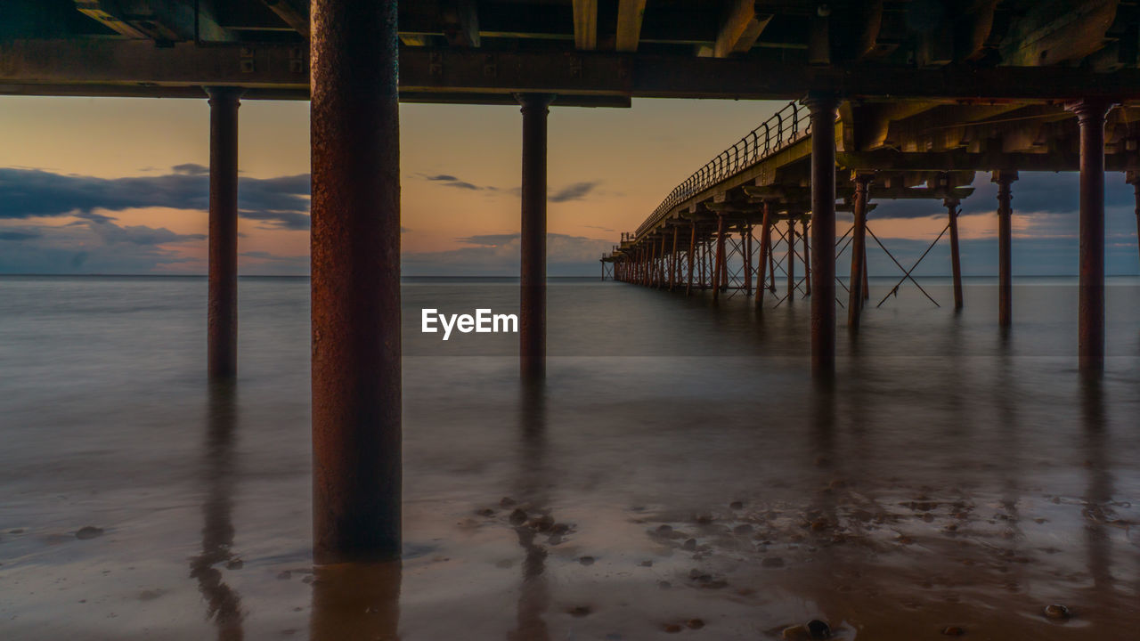 Sea below pier against sky during sunset