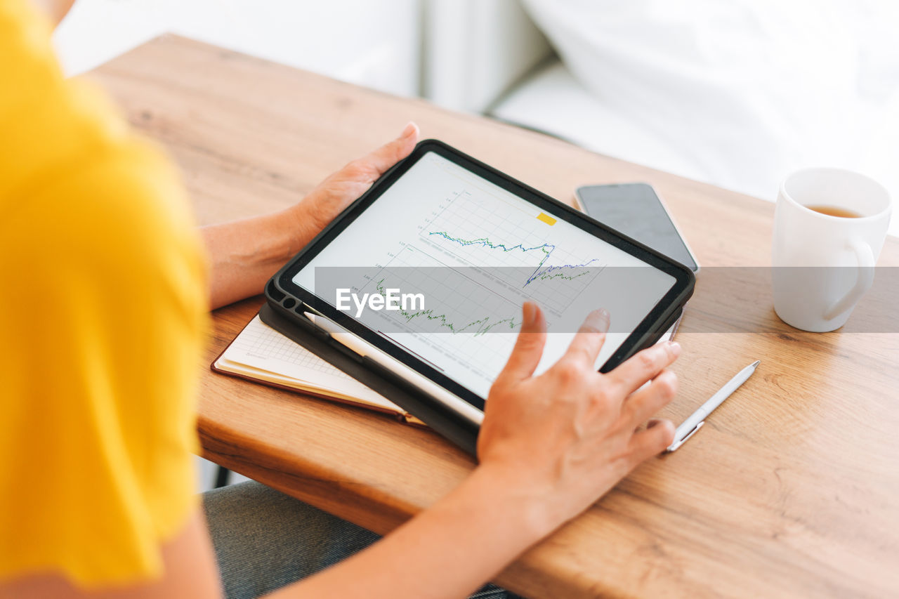 Young woman studies cryptocurrency charts and stock quotes on digital tablet with cup of tea at home