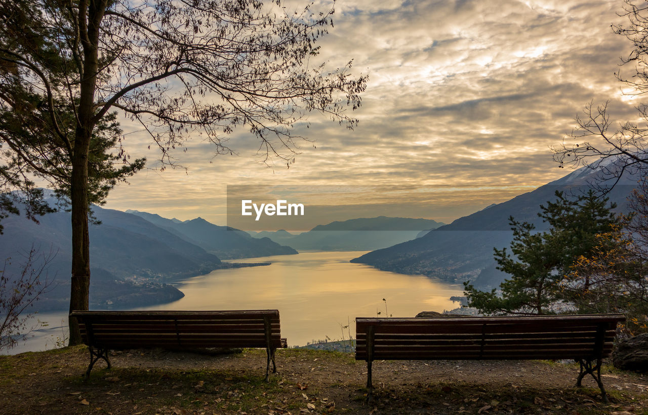 Empty bench by tree against sky during sunset