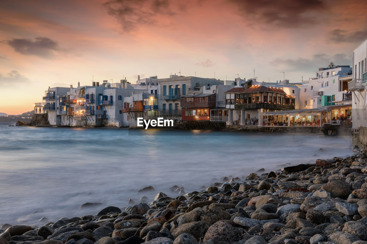 Buildings by sea against sky during sunset