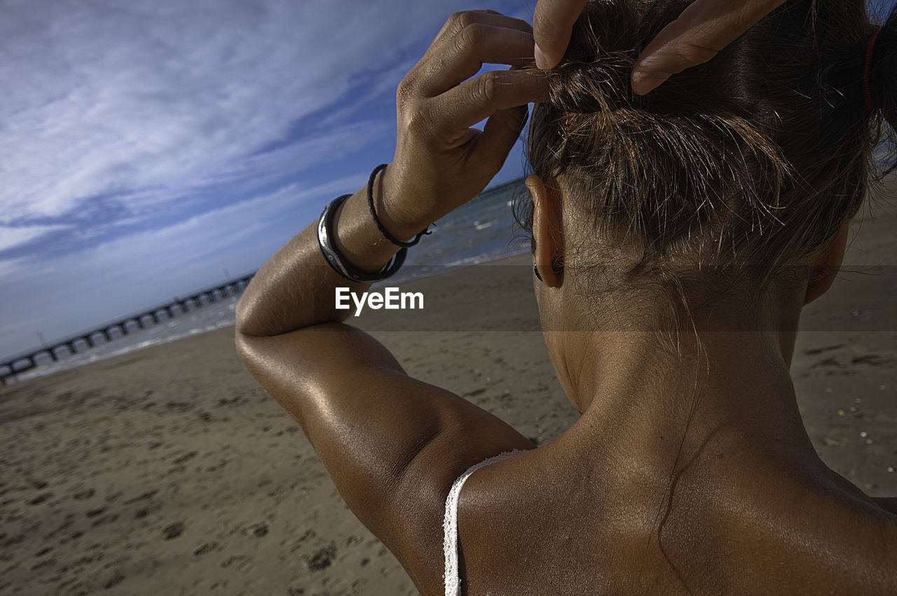 Rear view of woman tying hair at beach