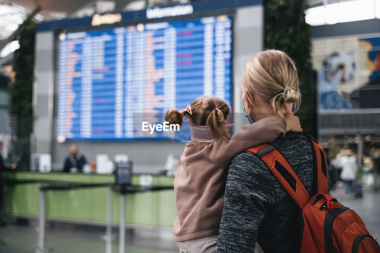 Man and girl watching timetable information at the airport, passengers waiting for a plane. family