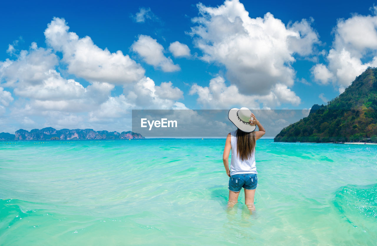 FULL LENGTH OF WOMAN STANDING IN SEA AGAINST SKY