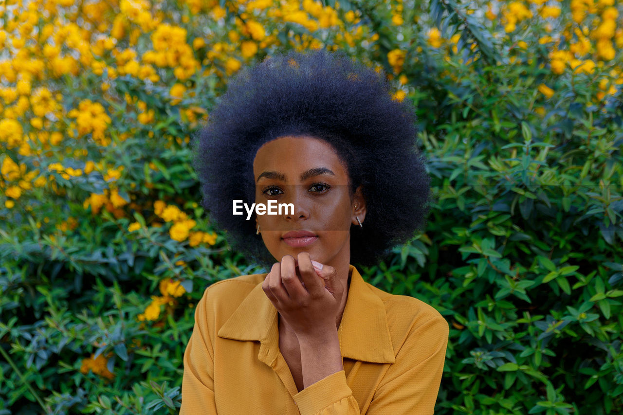 Portrait of woman with curly hair standing against yellow plants