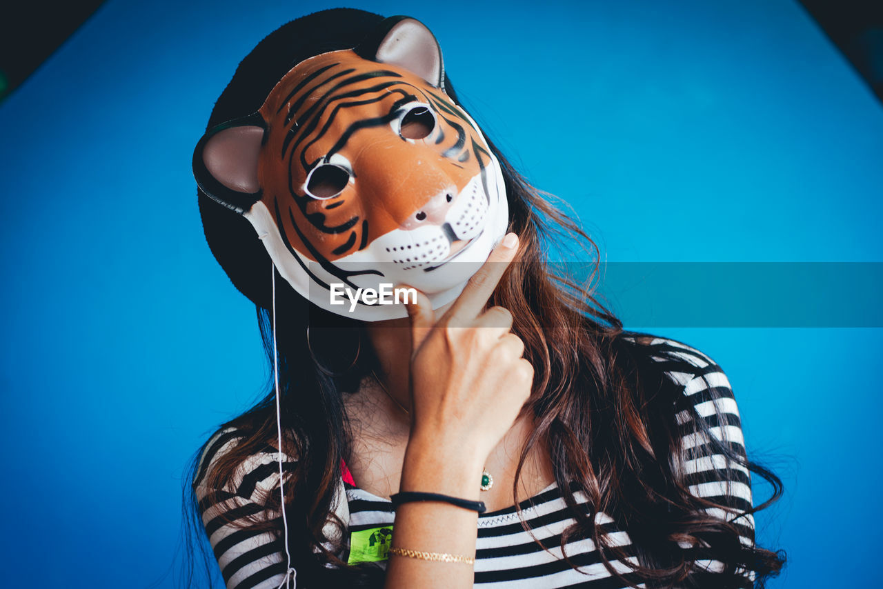 Portrait of woman wearing tiger mask against blue wall