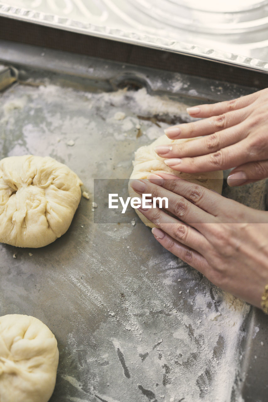 Cropped image of woman's hands kneading dough in tray at table