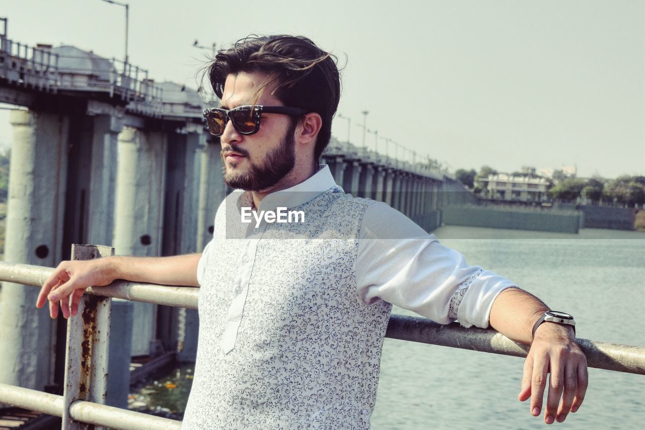 Man in sunglasses standing against lake and sky