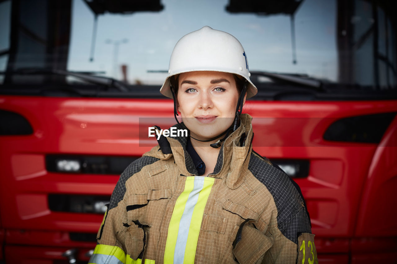 Portrait of female firefighter wearing helmet against fire engine at fire station