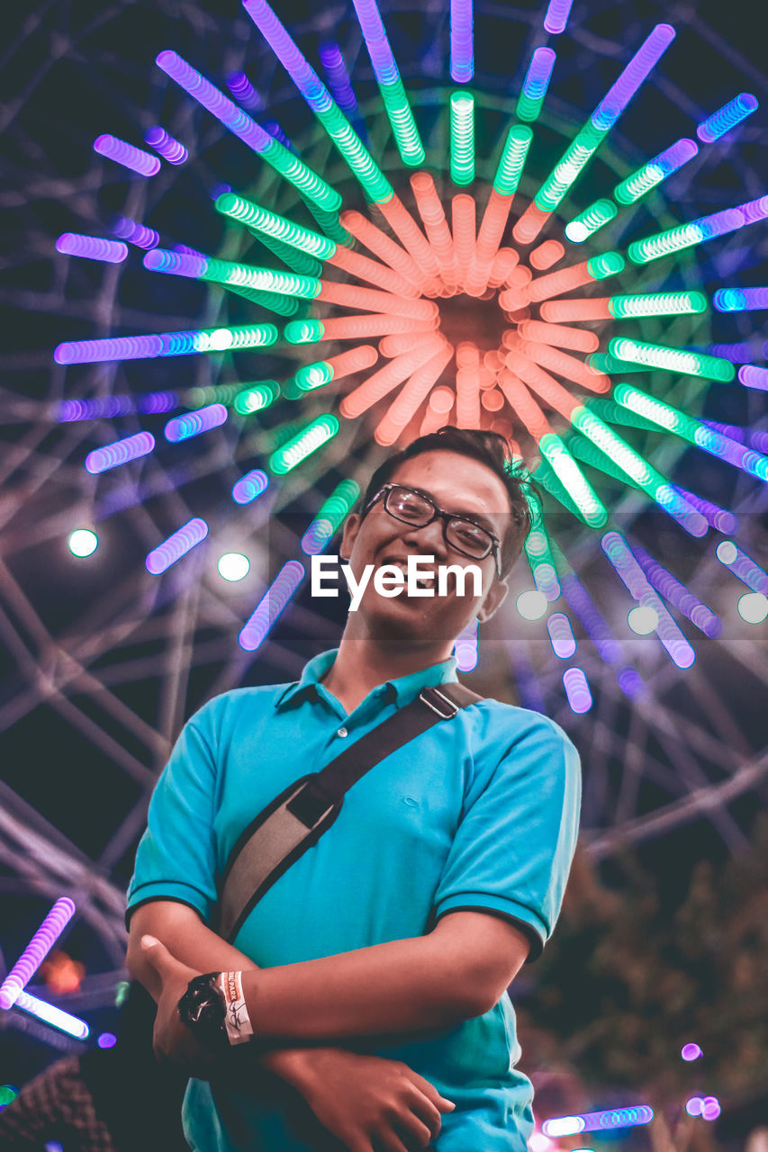 Portrait of smiling young man against illuminated ferris wheel