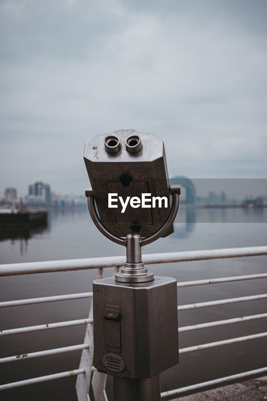 binoculars, coin-operated binoculars, coin operated, water, sky, railing, architecture, nature, city, surveillance, no people, cloud, day, observation point, travel destinations, sea, focus on foreground, outdoors, astronomy, tourism, telescope, built structure, light, travel, hand-held telescope, white, building exterior, security, technology, optical instrument