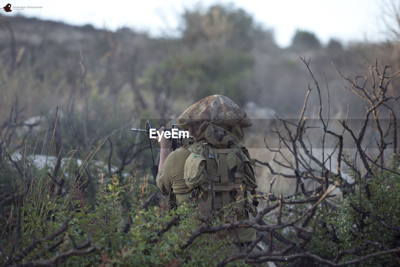Rear view of soldier aiming with sniper on field