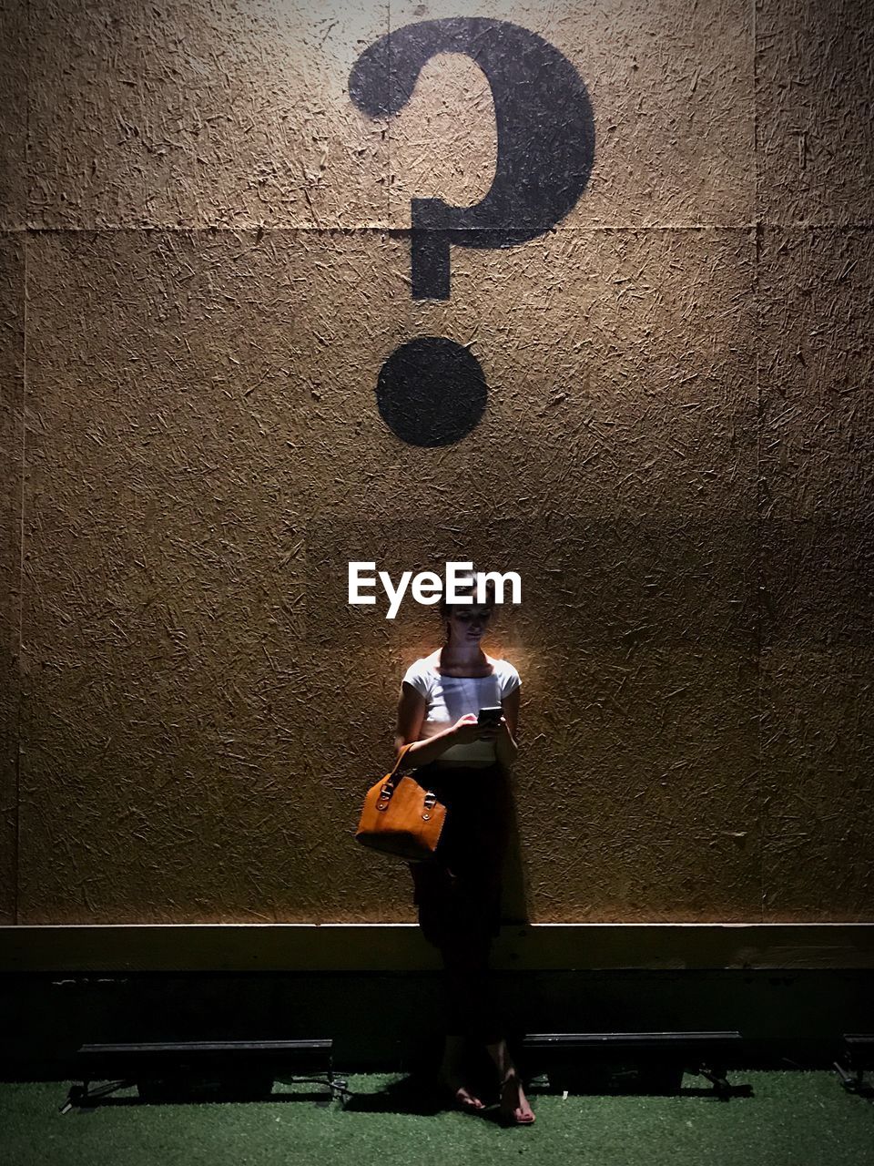 Woman using phone while standing below question mark on wall at night