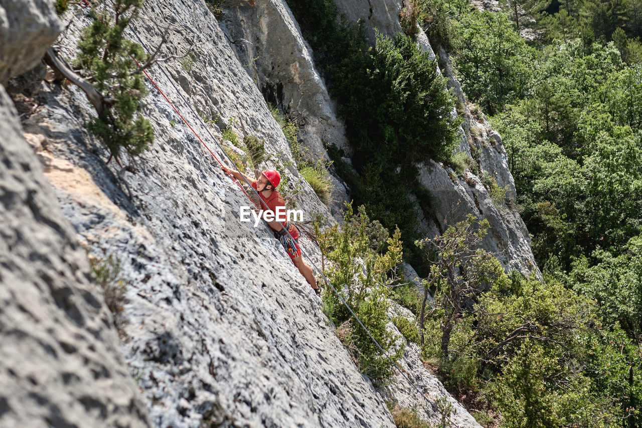 Side view of mountaineer in safety equipment climbing steep rock during summer vacation