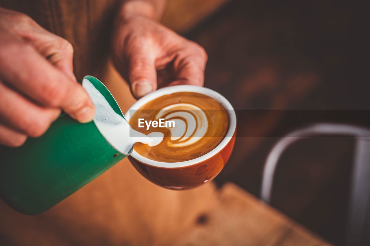 Cropped image of hand pouring milk into coffee cup