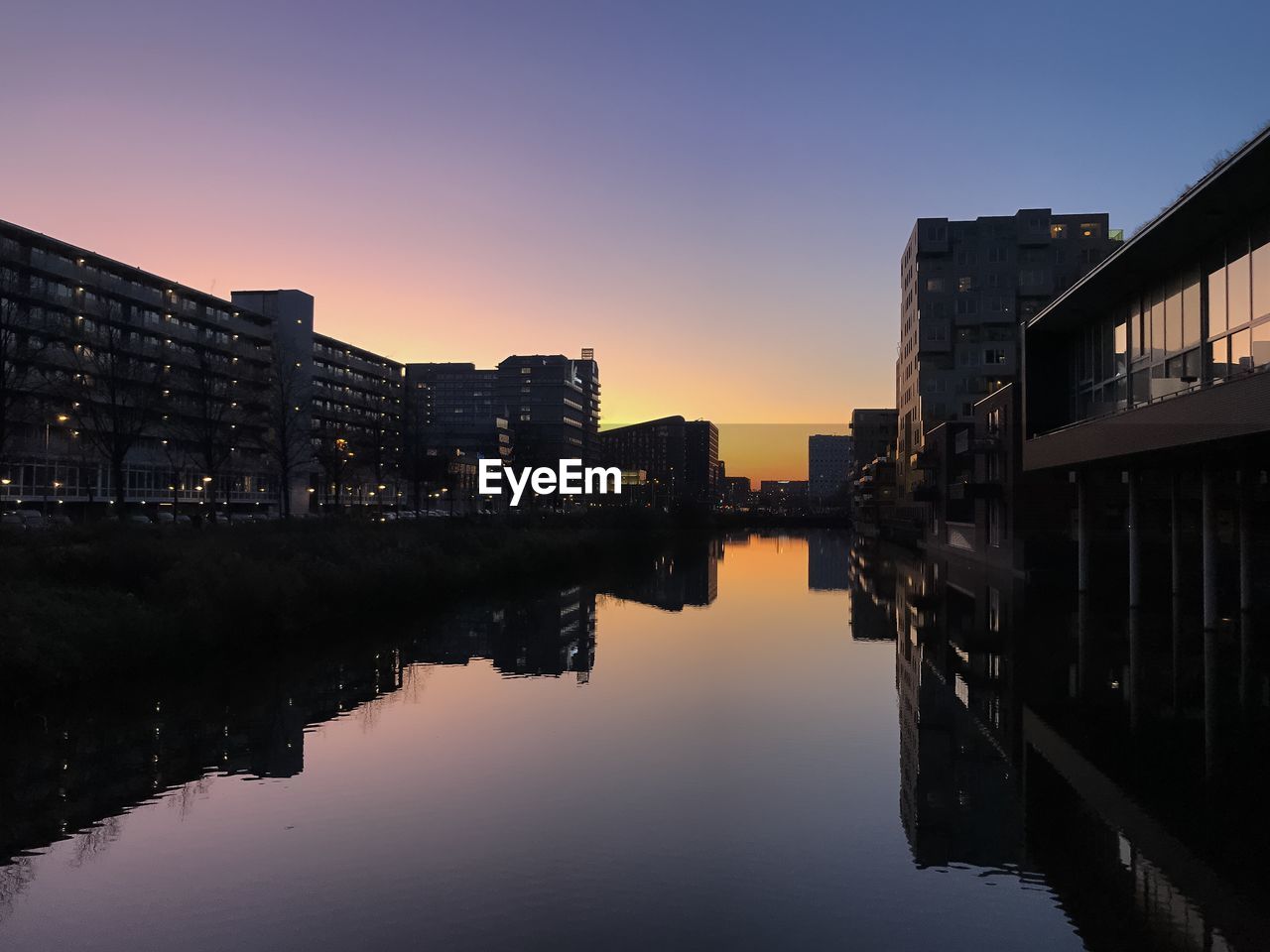 River amidst buildings against clear sky at sunset