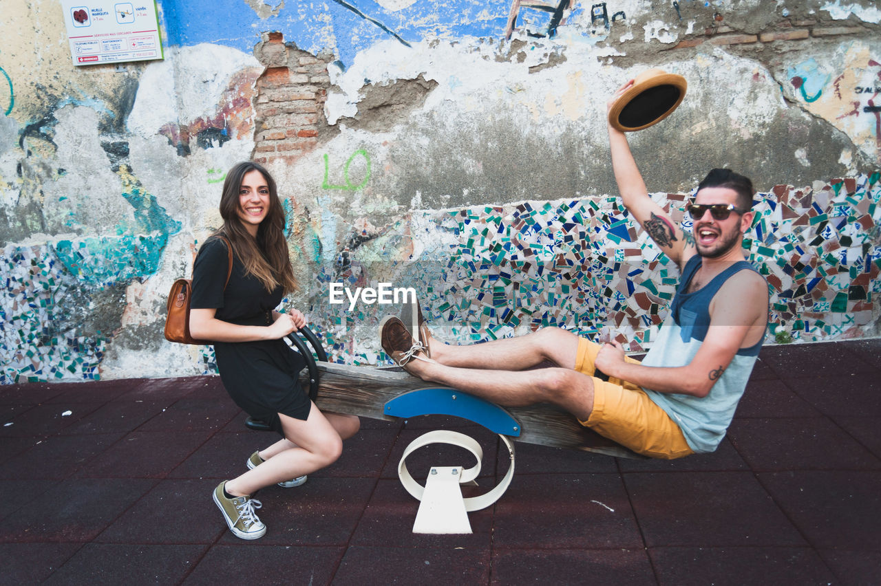 Happy friends playing seesaw against damaged wall