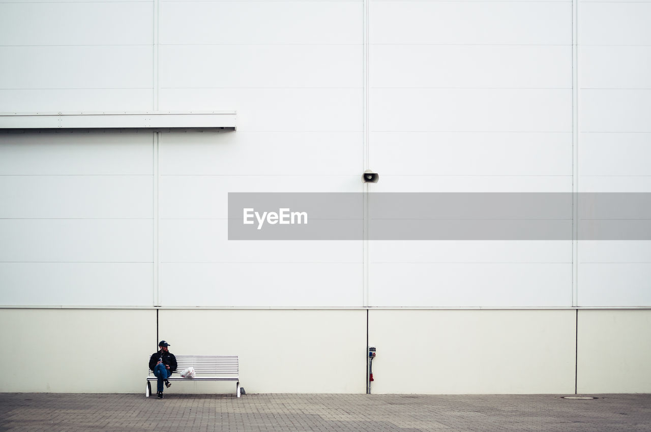 Man sitting on bench against white wall