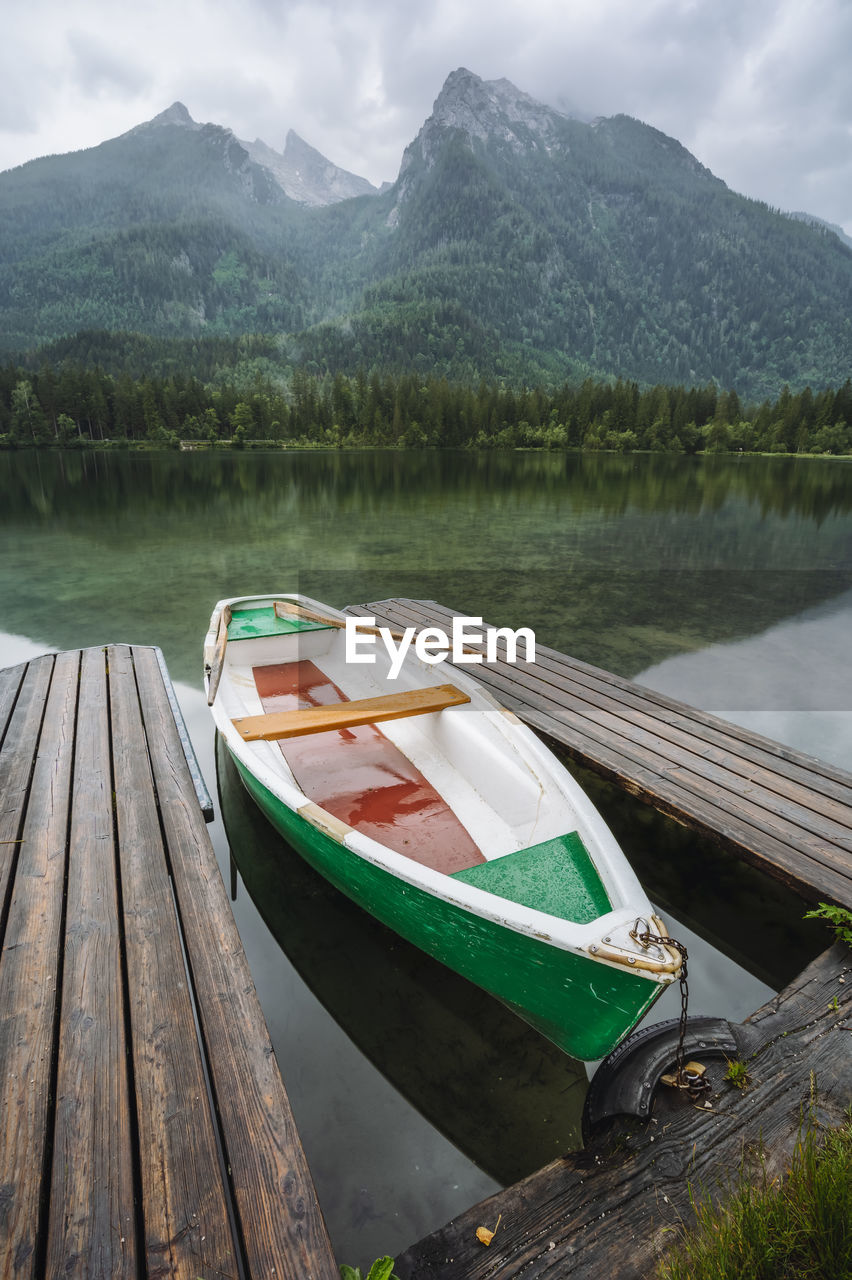 BOATS MOORED IN LAKE AGAINST MOUNTAIN RANGE