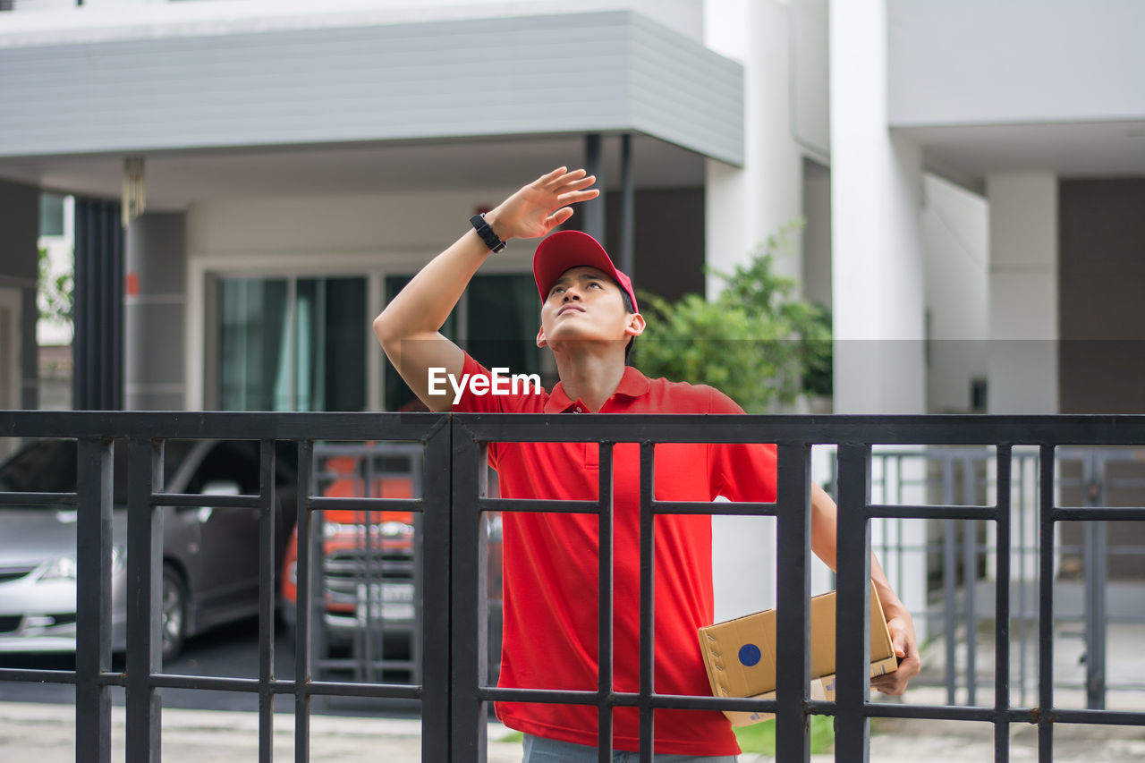 Delivery man standing at closed gate against buildings