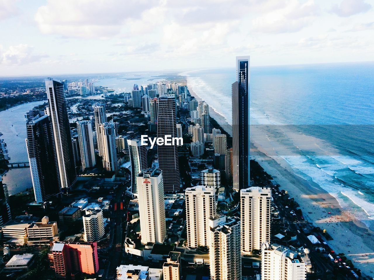 Aerial view of buildings by sea against cloudy sky