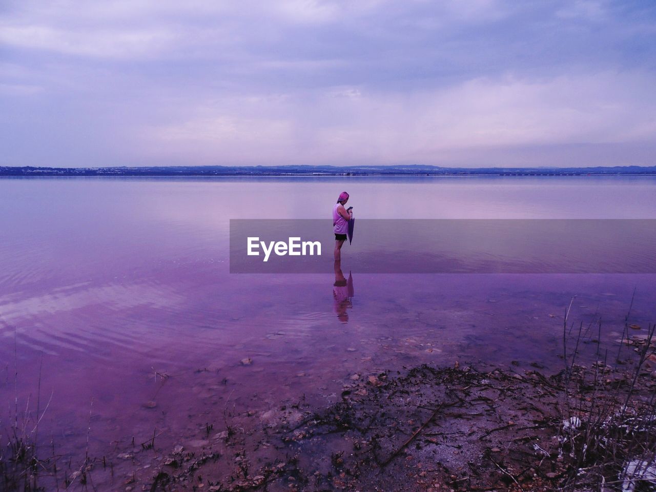 Woman standing in lake against sky during sunset