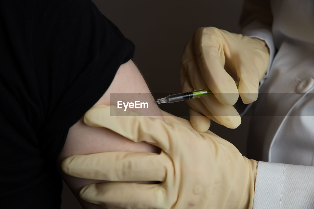 Midsection of doctor injecting syringe to patient against gray background